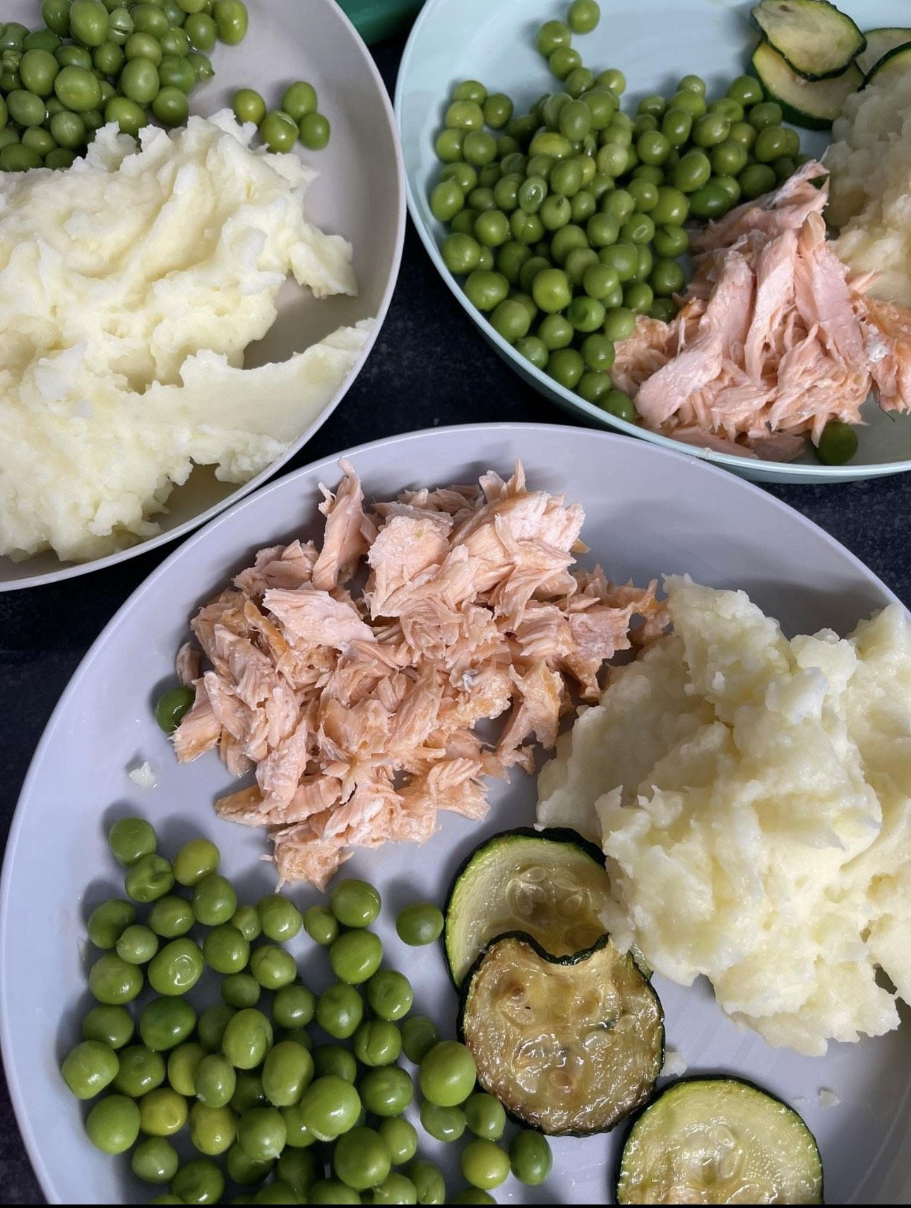 Freshly served plates of salmon, mash, peas and courgette